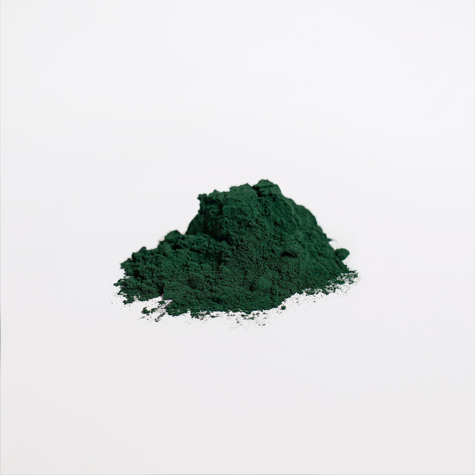 A small mound of nutrient-dense 111 & COMPANY SPIRULINA POWDER by Retro Fitness Supplements sits against a white background. The finely textured, dark green spirulina forms an uneven heap with scattered edges, its vibrant color contrasting starkly with the simplicity around it.