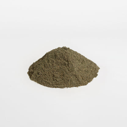 A small, conical mound of fine, dark green powder sits on a plain white surface. The smooth, matte texture is reminiscent of superfoods like the Ultra Cleanse Smoothie Greens from Retro Fitness Supplements 111 & Company line. The uniform white background highlights the powders vibrant hue.