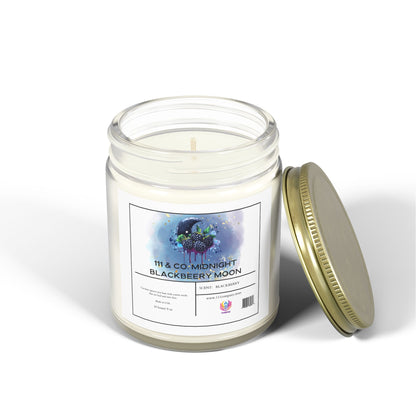 A clear glass jar candle with a lid from Printify lies open nearby. The label displays a colorful planet with trees under the text 111 & Co: Midnight Blackberry Moon. Made from coconut apricot wax, the white 9oz candle reveals its wick and emits a heavenly blackberry scent.